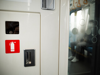 Safety fire extinguisher panel box with symbol in commuter subway train with passenger sitting on...