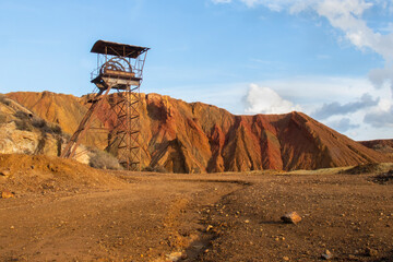 Abandoned mine pit head tower winch at Mazzarron Murcia Spain with red earth showing bright at dusk golden hour