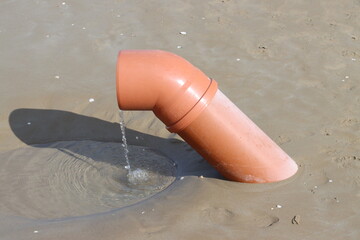 Drainage pipe pouring water on sandy beach creating small puddle