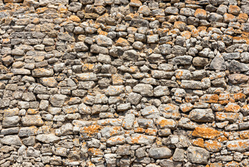 Texture of weathered stone wall showcasing vibrant orange lichen in a natural landscape