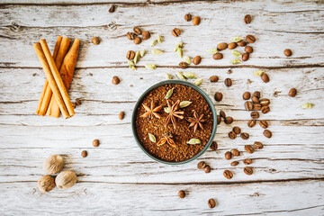 Ground coffee in rustic bowl garnished with star anise and cardamom, framed by cinnamon sticks, nutmeg and scattered beans on weathered wood — aromatic autumn chai-latte inspiration