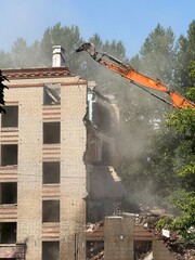 Dynamic image of an orange excavator in action, demolishing an old Soviet-style brick apartment building. Dust fills the air as the machine tears through walls, capturing the raw power of urban 