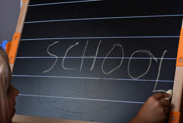 Little european style girl writing a word school with a chalk on the chalkboard.