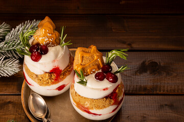 A glasses of Christmas dessert with gingerbread cookies, whipped cream and cranberries on wooden...