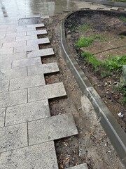 Damaged urban sidewalk with missing tiles and littered ground. Concept of infrastructure neglect, urban decay, and municipal maintenance issues