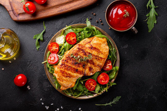 Grilled chicken breast with arugula and tomatoes i a plate and black background top view