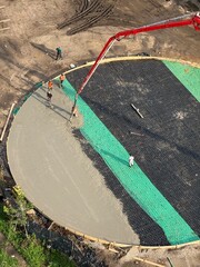 Aerial view of construction workers pouring concrete on a circular foundation with reinforced steel mesh and pump crane. Industrial development and civil engineering concept