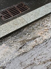 Rainwater flows along an urban street curb towards a storm drain. Concept of drainage system, infrastructure, and urban flood management