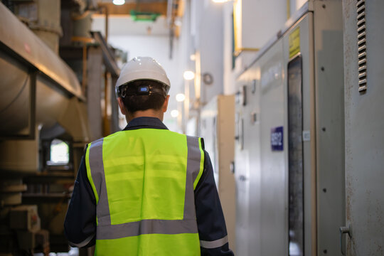 Gas insulated switchgear is monitored by worker in power station wearing safety helmet and reflective vest in industrial environment with electrical equipment and pipes