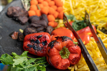 Grilled red bell peppers with meat, potatoes, and french fries on hot surface