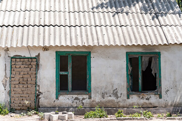 An old abandoned one-story house with broken windows and a doorway that is bricked up.