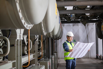 Gas insulated switchgear equipment in power station with engineer inspecting blueprint for...