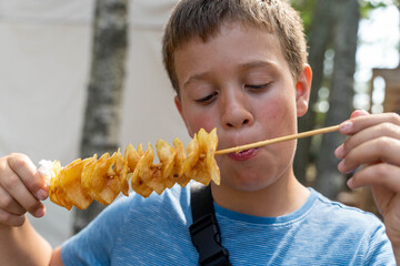 Boy eating tornado potato on a stick at summer festival