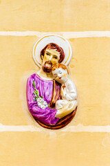 Religious Ceramic Relief Depicting Saint Holding a Child on Textured Wall