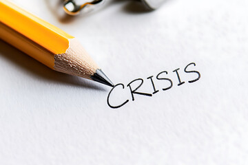 Pencil writing the word "crisis" on paper, suggesting challenges, problems, or difficult situations that need solving. Critical situation.