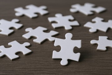 Close up of scattered white puzzle pieces on wooden surface with one piece connected in the center illustrating problem solving and teamwork concept