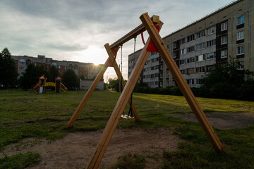 Empty swing set stands on playground in front of apartment building at sunset
