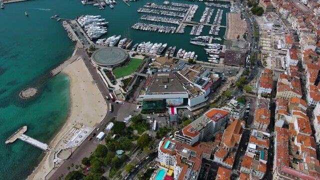 Top‑down drone shot of Cannes&rsquo; Palais des Festivals with the red carpet ready, La Croisette beach and a packed superyacht marina on the turquoise Mediterranean, France.