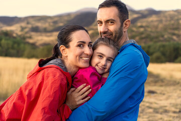 A happy family hugging and smiling at the camera in a beautiful field at sunset. A portrait of...