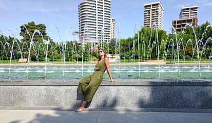woman in green jumpsuit is resting near the fontain in a hot summer day