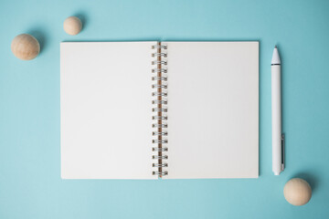 Workspace with empty notebook, pen and wooden ball on blue background.