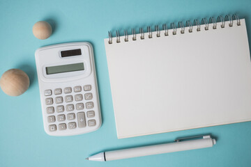 Workspace with empty notebook, calculator, pen and wooden ball on blue background.
