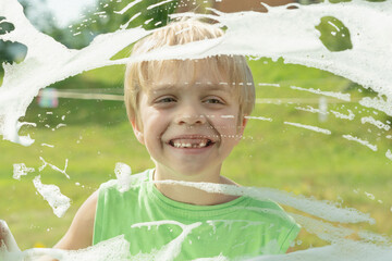 The boy happily looks out the window, which is smeared with soap suds.