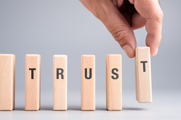 A hand putting the final block of the word TRUST, showing that trust is built piece by piece and requires consistent actions and integrity