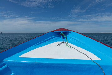 Colorful boat sailing on a calm sea with sand dunes and a navigation aid visible in the distance,...