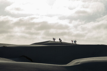 Tourists walking across expansive sand dunes under a cloudy sky, immersing themselves in the beauty of the vast desert landscape