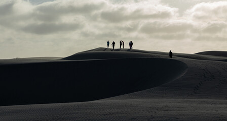 Tourists walking on sand dunes under a cloudy sky, creating a dramatic and adventurous atmosphere