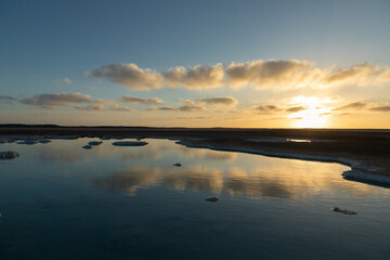 Sunset clouds mirroring calm saltwater with surrounding arid landscape and sandy terrain