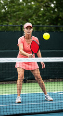 senior woman on pickleball court playing ball with paddle over the net