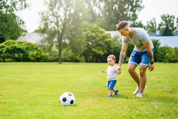 Young father with his little son playing football on football pitch