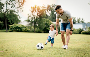 Young father with his little son playing football on football pitch