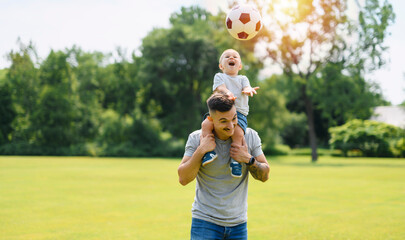 Young father with his little son playing football on football pitch
