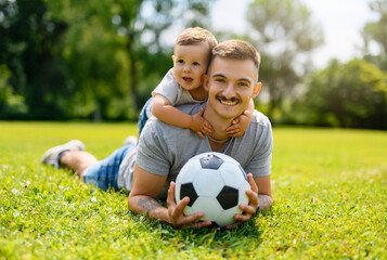 Fototapeta premium Young father with his little son playing football on football pitch