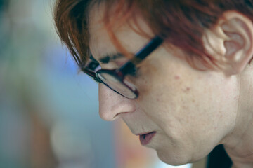Close up portrait of an artist with red dyed hair and glasses concentrating intently on their work...