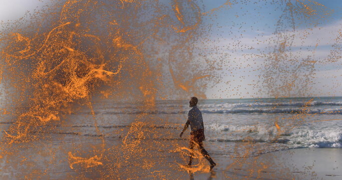 Mature African American man walking along wet shoreline by waves, with orange sparks, copy space