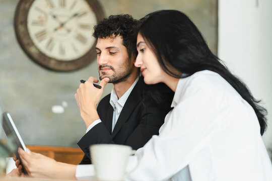 Two business professionals in office loft style using digital tablets discussing or meeting. Hispanic man and woman collaborating on work project. small business, lifestyle working in home office