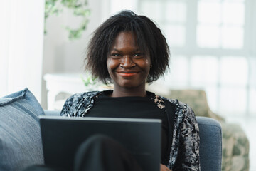 Business, working, technology, Black woman freelancer smiling while using laptop at home, relaxed on sofa, representing confident online work, independent entrepreneurship and remote lifestyle