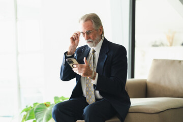 Senior businessman in formal shirt holding smartphone, appearing stressed during phone call lay off...
