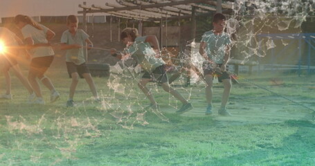 Pulling children gripping braided rope on grassy playground field under sun, with wooden play bars