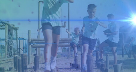 School age boy jumping across wooden post in outdoor obstacle course with clipboard