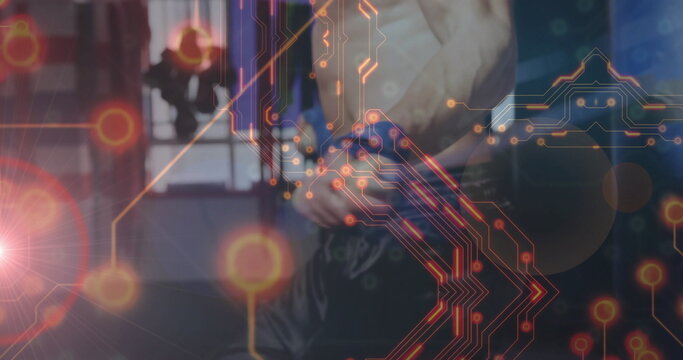 Shirtless fighter adjusting pants, tying printed belt in gym with punching bag and digital overlay - Powered by Adobe