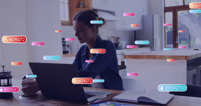 Working woman in denim shirt typing on laptop in home kitchen, with floating data tags