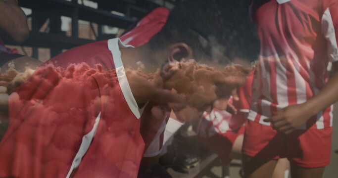 Sitting soccer player wearing red and white uniform hunching on sideline metal bench with bleachers