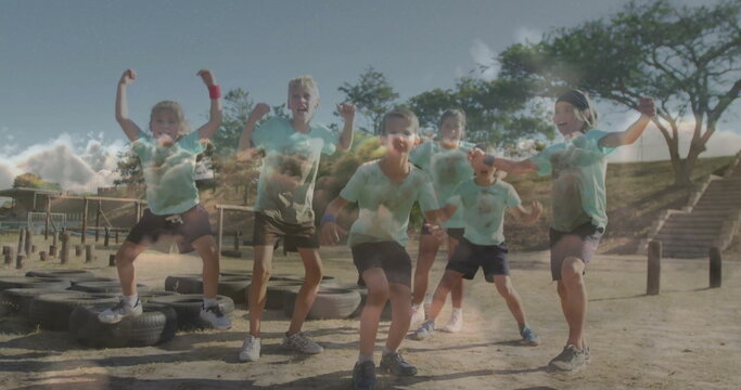 Flexing children wearing light blue shirts and shorts at park obstacle course, with tires