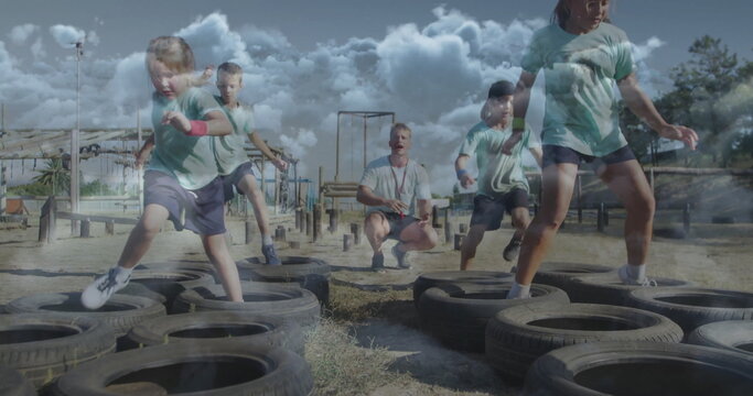 Training coach guiding children navigating tire obstacle course at outdoor park, in green shirts