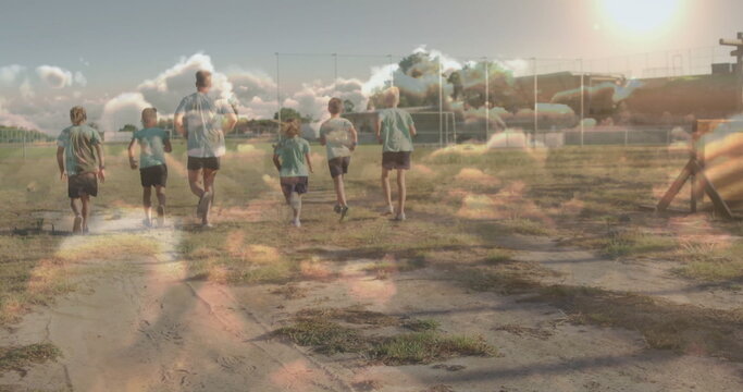 Fototapeta Jogging coach and children wearing shorts and t-shirts across sports field, with soccer goal frames